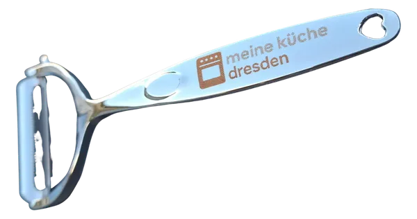 Stainless steel vegetable peeler with "meine küche dresden" logo engraving on the handle.